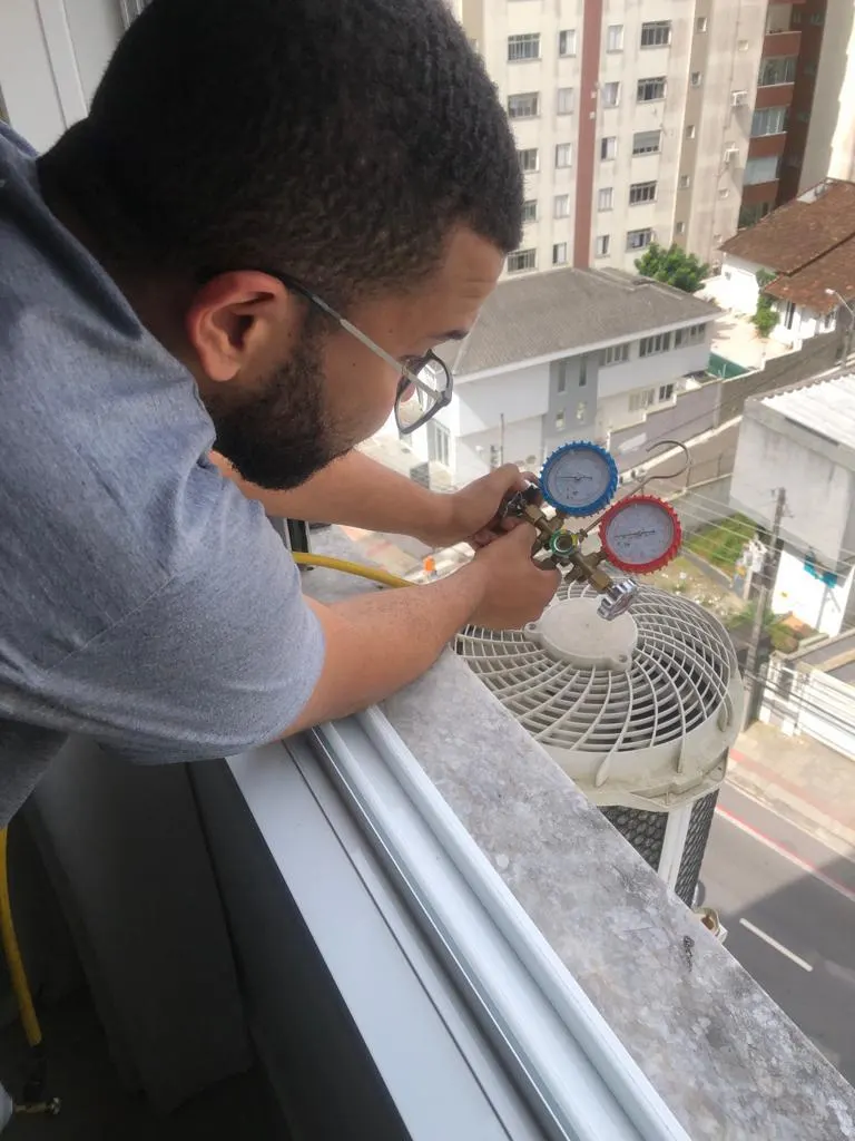 Técnico conferindo manômetros em condensadora na varanda de um prédio em Florianópolis