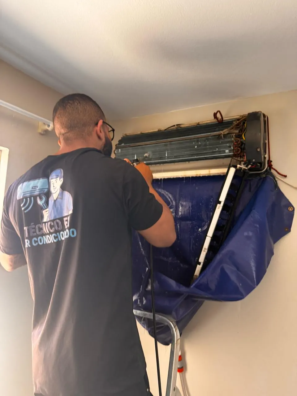 Técnico higienizando a evaporadora de um ar condicionado split com lona azul em Florianópolis